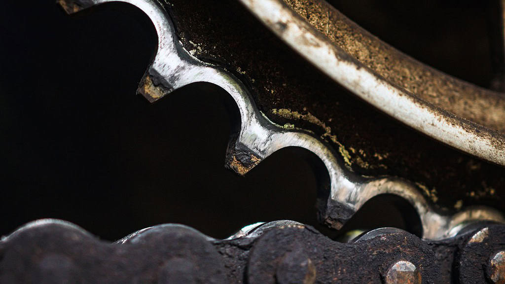 Rozsdás lánckerék részlete, szögletes fogazású fogak és olajozott felületek a kerékpár takarításához és karbantartásához.